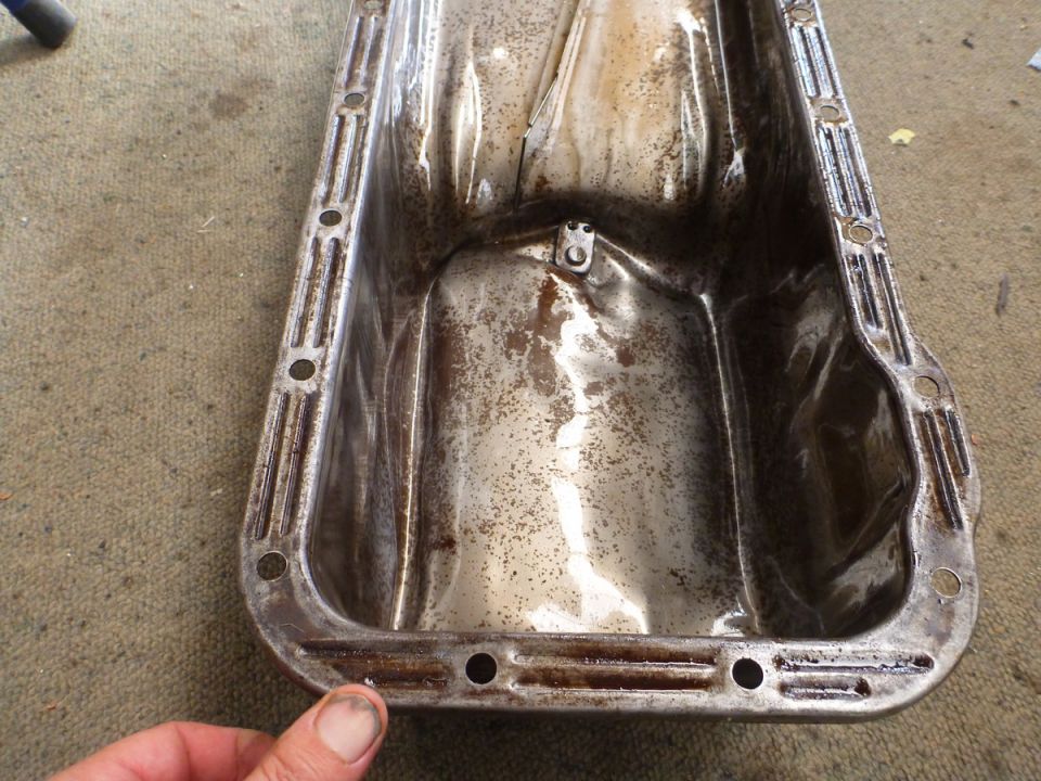 Dirty metallic oil pan with rust and grime, hand in corner
