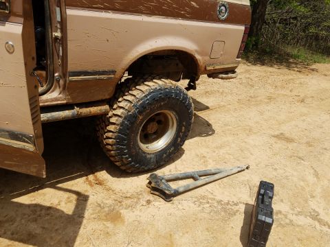1988 Ford Bronco - The rear driver's side of a dirty, tan and brown Ford Bronco is shown, with the driver's door open. A metal recovery arm and a black toolbo…