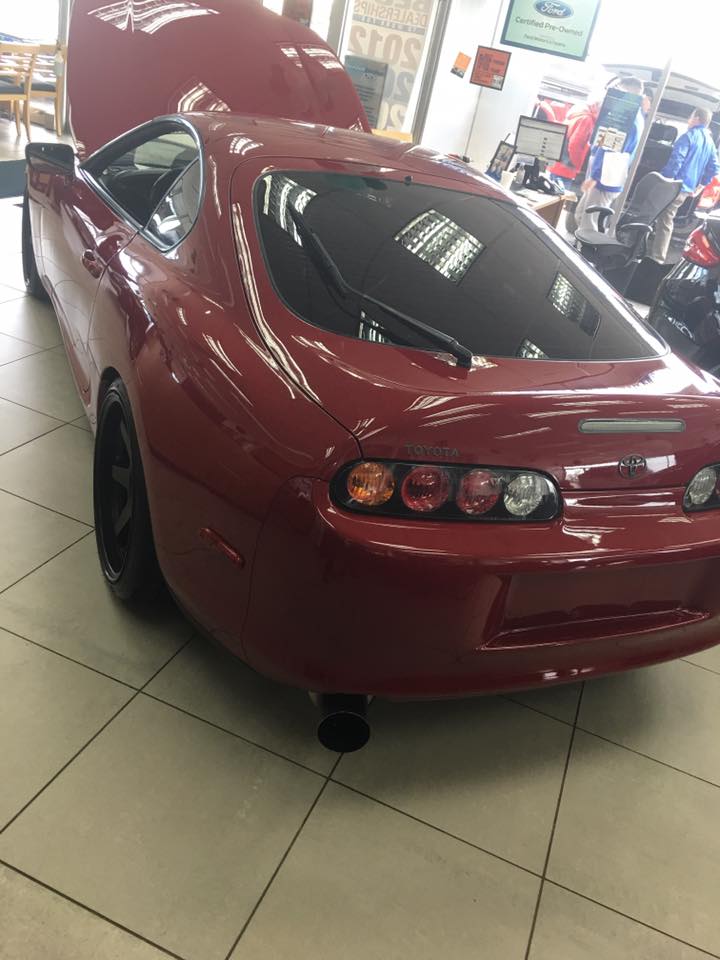 Dark red Toyota Supra, rear driver's side quarter view, hood open, indoors.