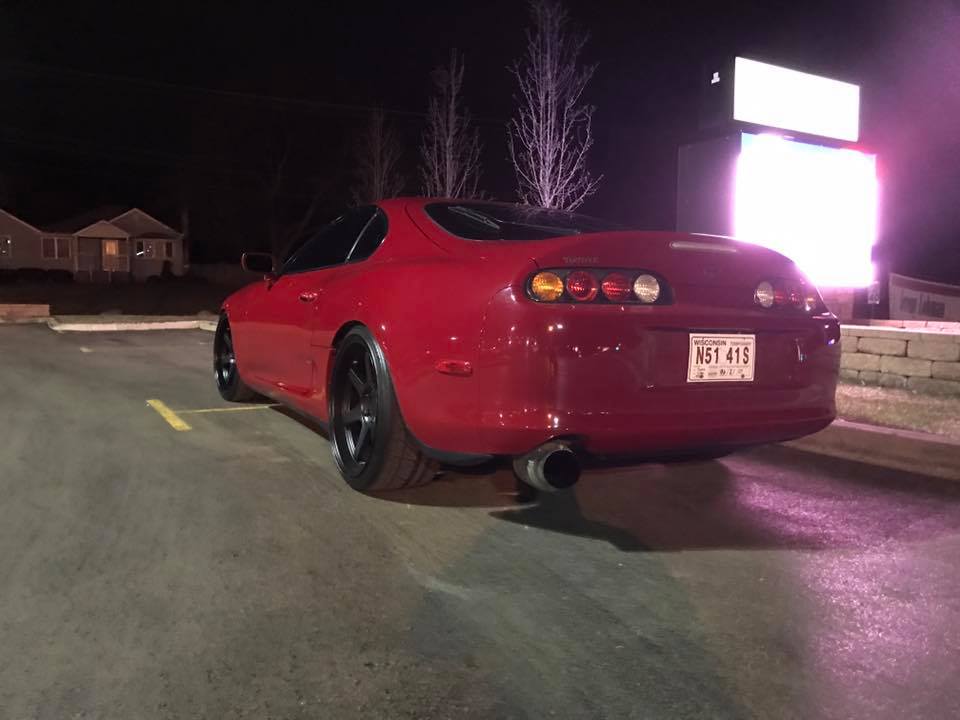 Red Toyota Supra parked at night, rear driver's side view.