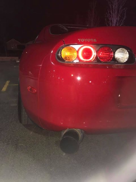1994 Toyota Supra - The rear of a red 1994 Toyota Supra is visible, showing its distinctive taillights and exhaust.