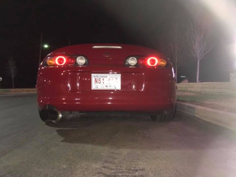1994 Toyota Supra - The rear of a red 1994 Toyota Supra is shown at night, its distinctive taillights and dual exhaust pipes.