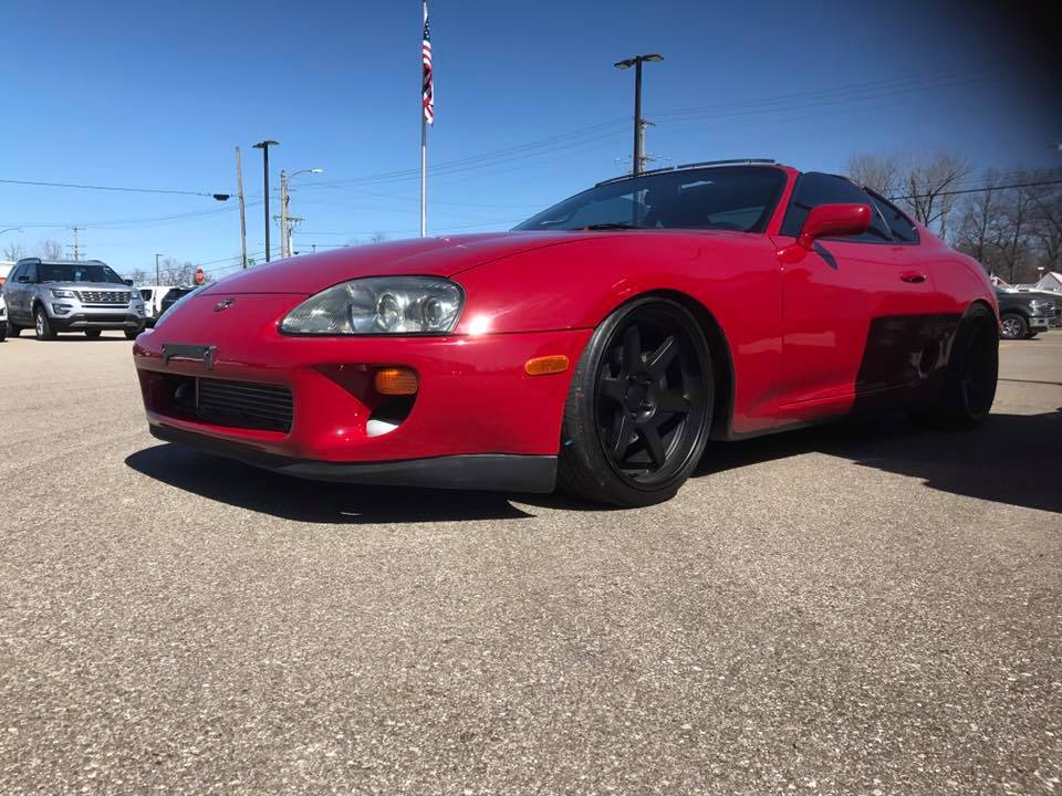 Red 1994 Toyota Supra parked on asphalt, front quarter view. Another SUV is visible in the background