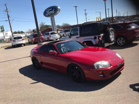 1994 Toyota Supra - A red 1994 Toyota Supra is parked in a lot with other vehicles under a Ford dealership sign.