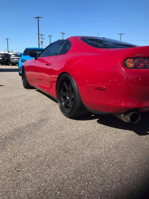1994 Toyota Supra - A red sports car is parked outdoors next to a blue vehicle, with a clear blue sky above.