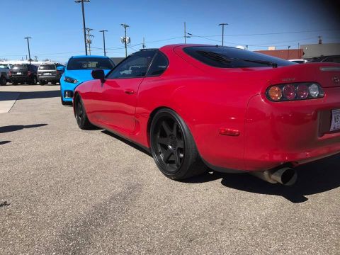 1994 Toyota Supra - A red 1994 Toyota Supra is parked in a lot, showing its distinctive taillights and aftermarket wheels.