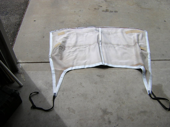 White vinyl soft top laid out inside-up on a concrete floor, showing bound edges and black tie-down straps
