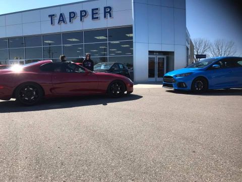 1994 Toyota Supra - Two cars, a red sports car and a blue hatchback, are parked outside a dealership with 'TAPPER' visible on the building.