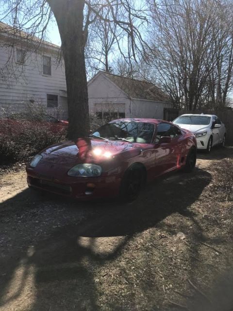 1994 Toyota Supra - A red Toyota Supra is parked in a driveway next to a white car, with a house and garage in the background.