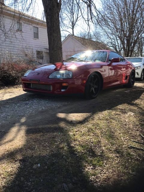 1994 Toyota Supra - A red sports car is parked in a driveway on a sunny day, with a white car visible in the background.