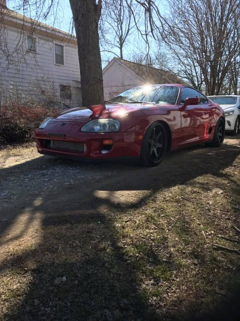 1994 Toyota Supra - A red Toyota Supra is parked outside a house with another vehicle behind it.