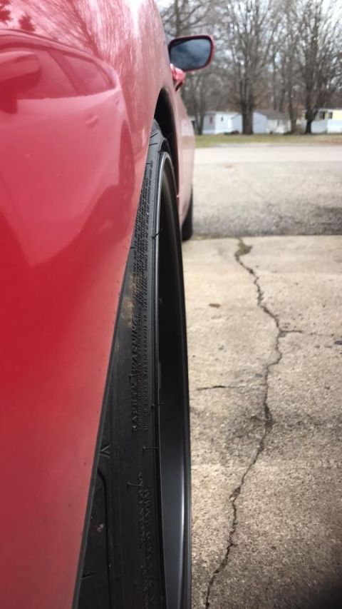 1994 Toyota Supra - Close-up side view of a red car's rear wheel and fender, showing a black rim and tire.