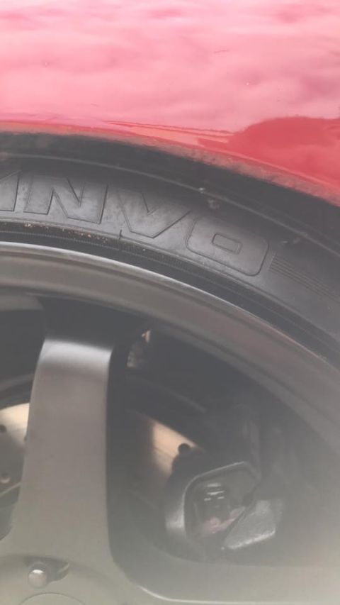 1994 Toyota Supra - Detail shot of a red car's wheel and fender area, with partial tire text visible.
