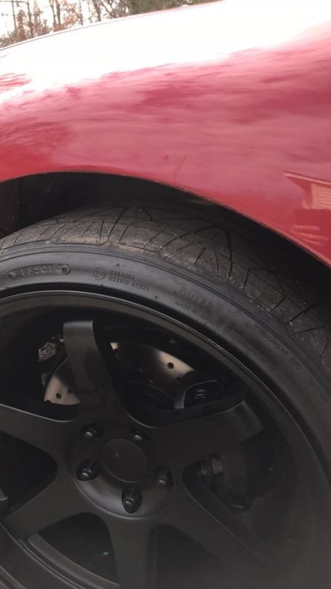 1994 Toyota Supra - This image shows a close-up of a red vehicle's fender and a black aftermarket wheel with drilled brake rotors.