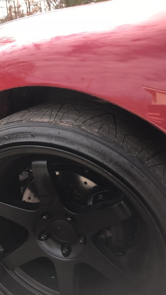 close-up of a red car's front fender and black aftermarket wheel with drilled rotors