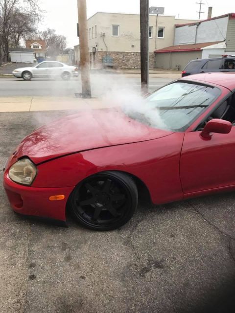 1994 Toyota Supra - A red 1994 Toyota Supra appears to be overheating, with smoke rising from under its hood.