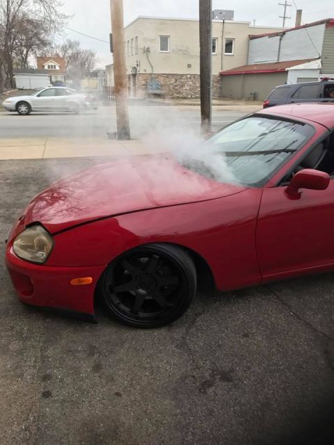 1994 Toyota Supra - A red sports car is seen with smoke emanating from its hood, suggesting mechanical trouble.