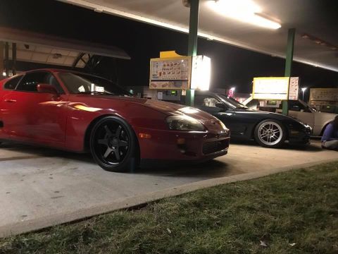 1994 Toyota Supra - A red 1994 Toyota Supra is parked next to other vehicles under a covered area at night.