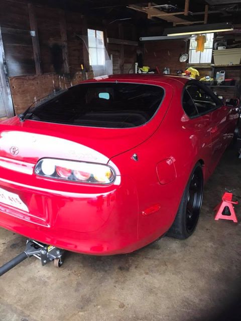 1994 Toyota Supra - A red 1994 Toyota Supra is seen in a garage, supported by a floor jack and jack stands.