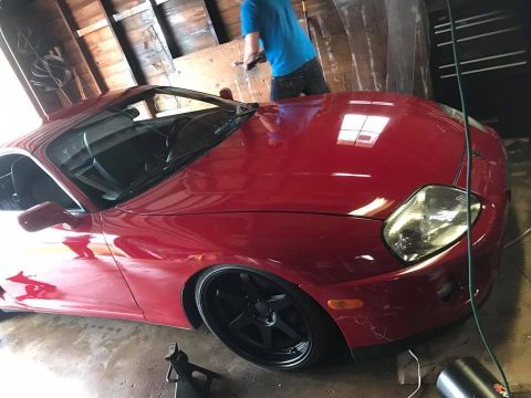 1994 Toyota Supra - A red 1994 Toyota Supra is shown in a garage, aftermarket black wheels and a lowered stance.