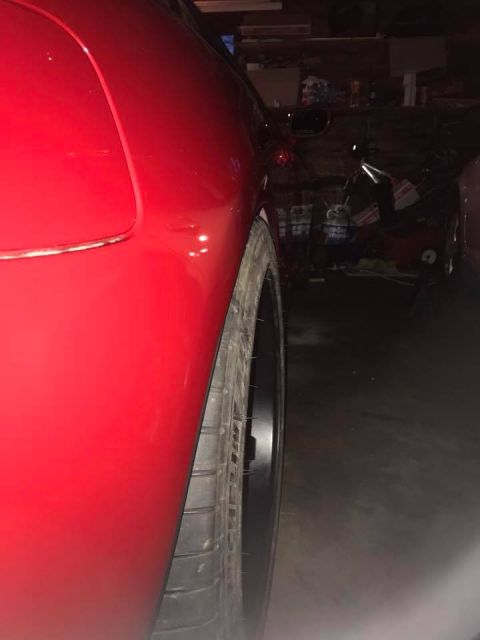 1994 Toyota Supra - A close-up view of the rear wheel and fender of a red sports car in a dimly lit garage.