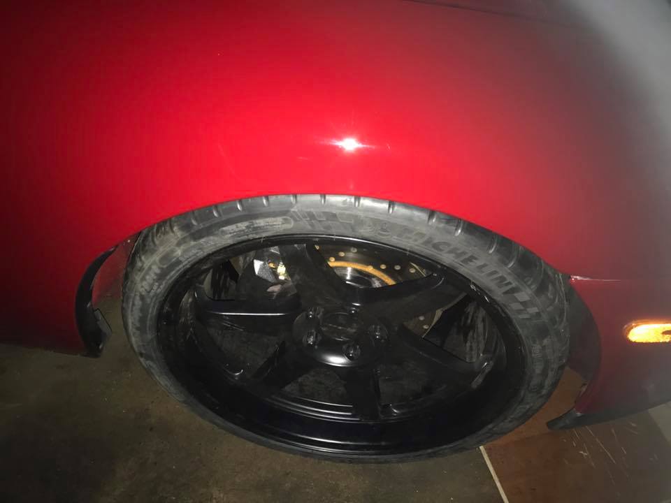 Red car's black aftermarket wheel and tire, with gold brake caliper visible