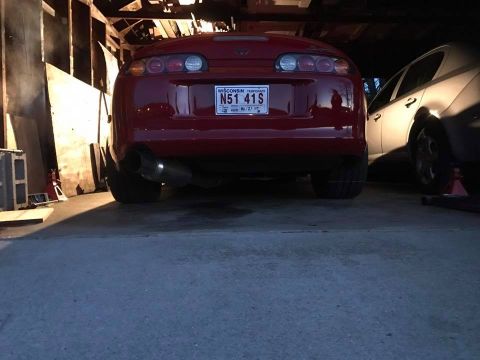 1994 Toyota Supra - Rear view of a red 1994 Toyota Supra parked in a garage, showing its distinctive taillights and custom exhaust pipe.
