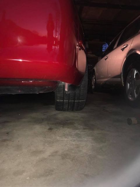 1994 Toyota Supra - A close-up view of a red vehicle's rear tire and lower body panel, with another car visible in the background.