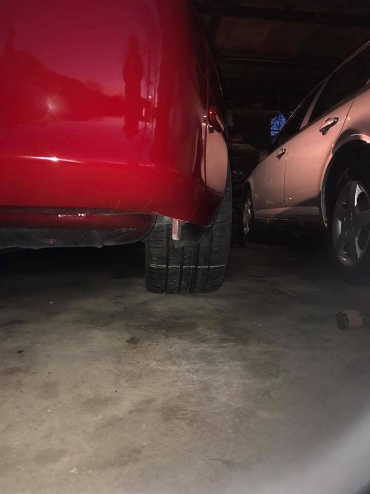 Red car's rear tire and quarter panel, parked next to a white car in a garage