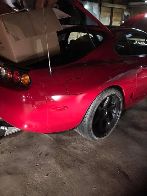 1994 Toyota Supra - The rear of a red 1994 Toyota Supra is shown with its trunk open, revealing a large cardboard box.