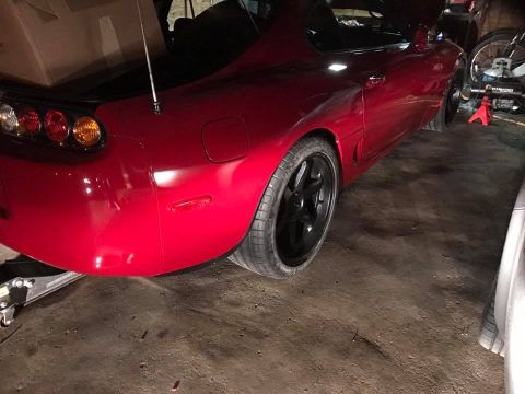 1994 Toyota Supra - Rear view of a red Toyota Supra with aftermarket wheels and taillights, parked indoors.