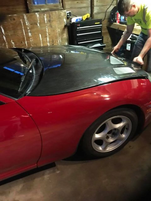 1994 Toyota Supra - A person works on the carbon fiber hood of a red sports car in a garage.