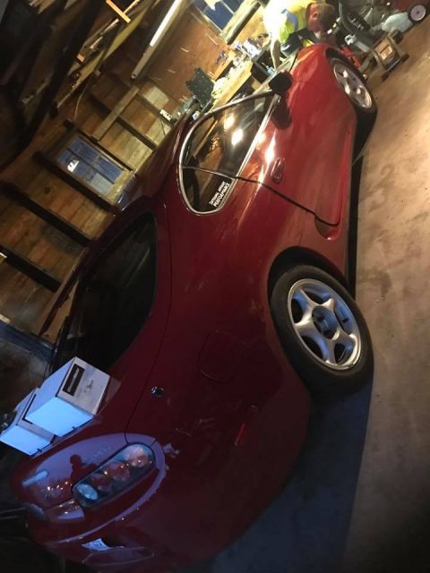 1994 Toyota Supra - A red sports car is parked indoors, showing its 3/4 front profile with aftermarket wheels and a sticker on the window.