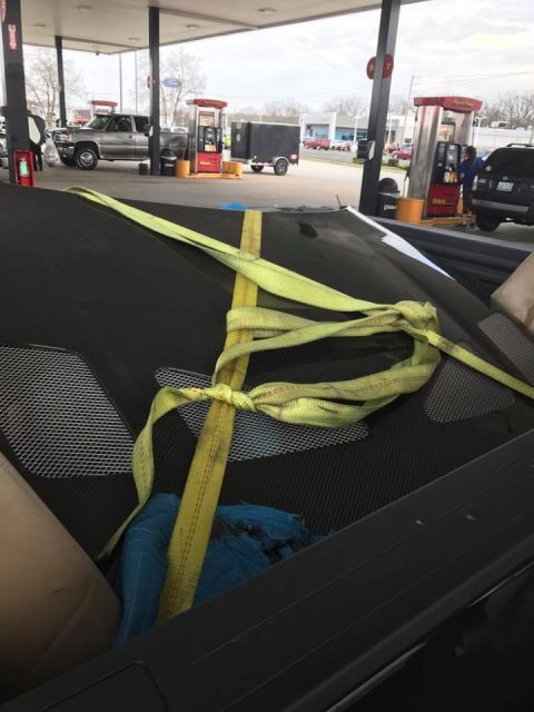 1994 Toyota Supra - A car hood is secured with yellow straps while at a gas station with other vehicles present.