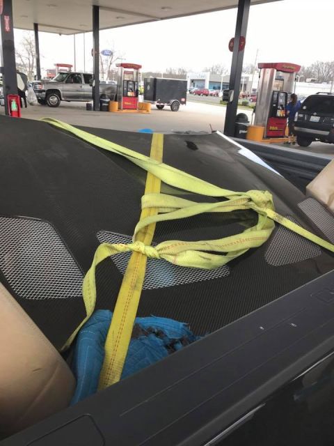 1994 Toyota Supra - A car hood is strapped down at a gas station, with other vehicles and pumps visible in the background.
