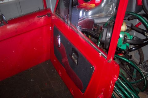 1974 Ford Bronco - Close-up view of the red interior door panel and frame of a vehicle, showing the door handle and part of the interior.