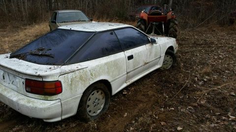 1988 Toyota Celica - This white 1988 Toyota Celica coupe, viewed from a 3q-front angle, is covered in dirt and debris.
