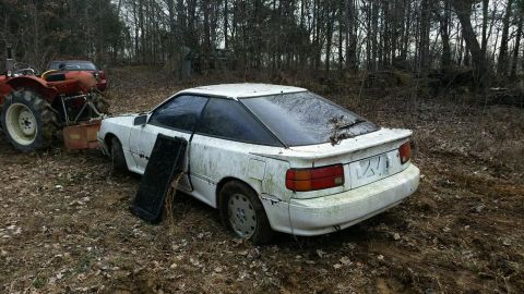 1988 Toyota Celica - White 1988 Toyota Celica stuck in a muddy field, with a tractor preparing to tow it.