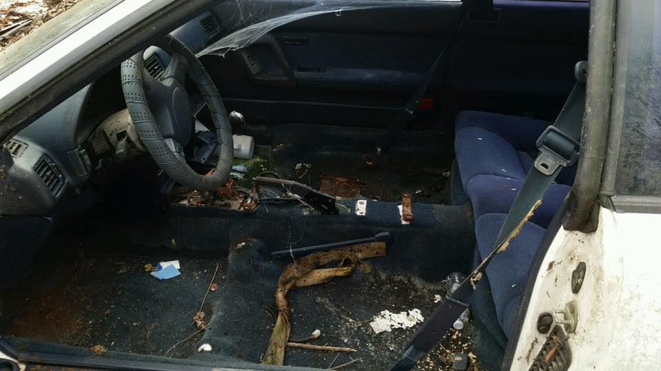 Interior of a dirty car with ripped seats and debris on the floor