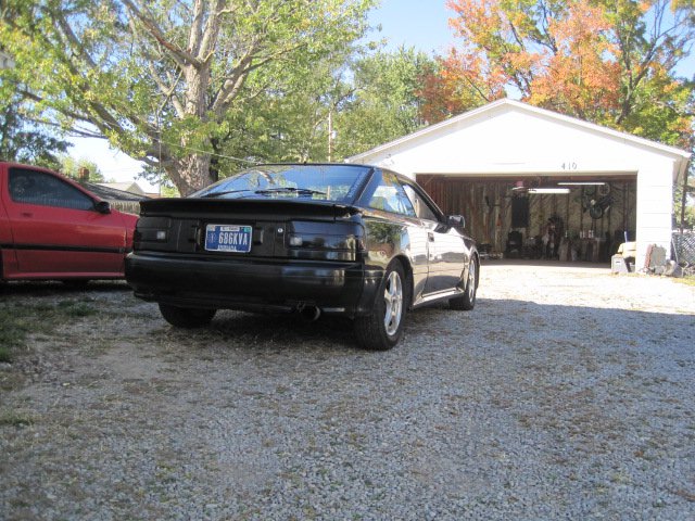black coupe with spoiler, parked next to red car in front of garage