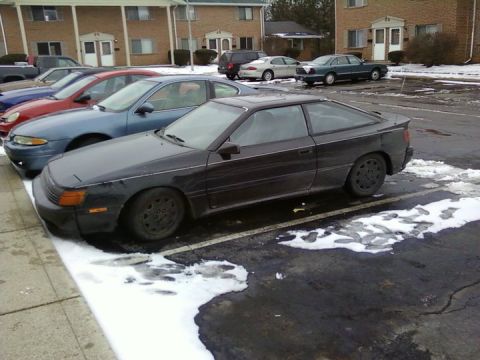 1988 Toyota Celica - A dark coupe with pop-up headlights is parked in a lot with snow on the ground.