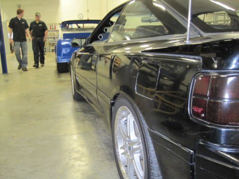 1988 Toyota Celica - A black car with custom wheels and tinted taillights is parked indoors next to another vehicle.