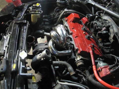 1988 Toyota Celica - Close-up of an engine bay a red Toyota valve cover and custom exhaust manifold.