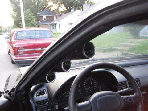 1988 Toyota Celica - The dashboard of a car displays aftermarket gauges, with a red sedan visible through the windshield.