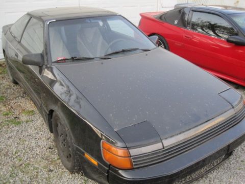 1988 Toyota Celica - A black 1988 Toyota Celica coupe is parked next to a red sports car.