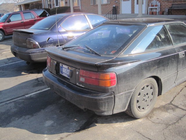 Black coupe with a rear spoiler and a "Turbo" badge, seen from the rear