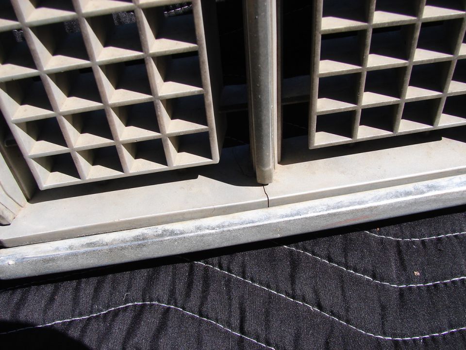 Close-up of a beige plastic ventilation grille with a metal trim piece below it, resting on a black quilted fabric