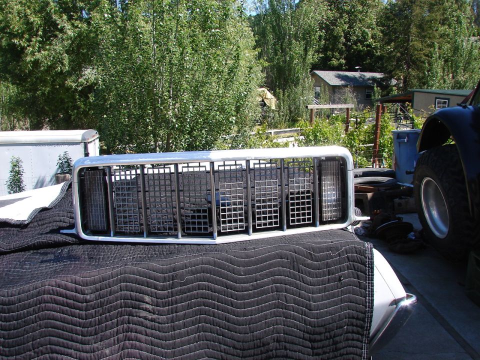 Chrome and black vehicle grille with square openings, sitting on a quilted black cover