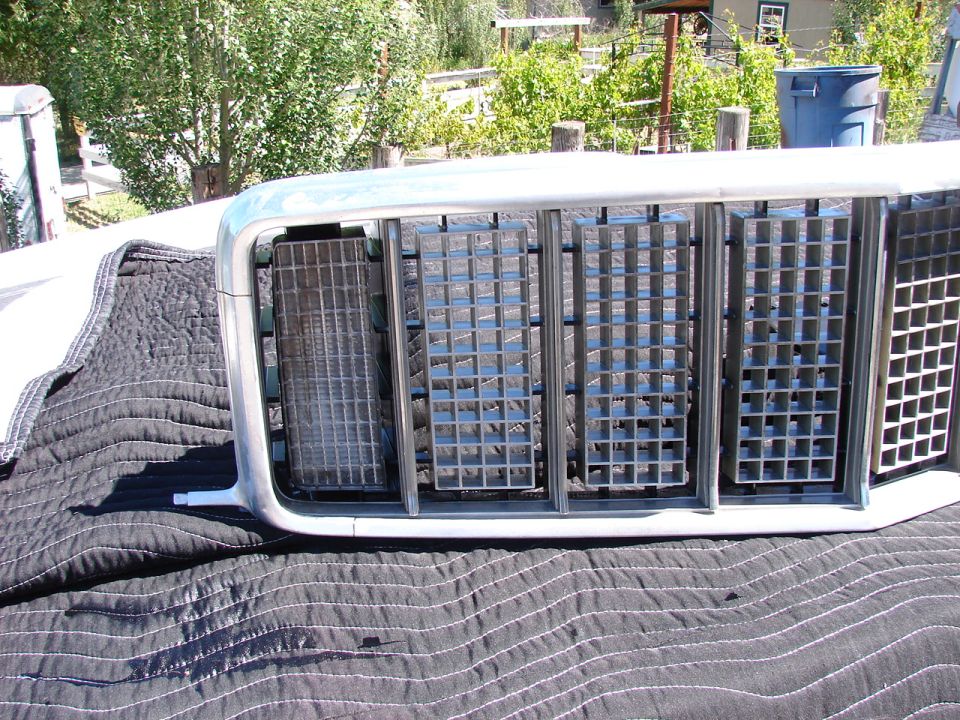 Chrome and silver car grille with multiple square openings, resting on a quilted black cover