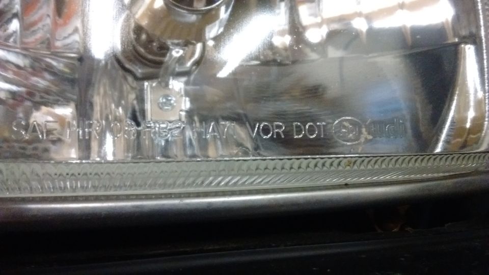 Close-up of clear headlight lens with SAE and DOT markings and Audi logo embossed